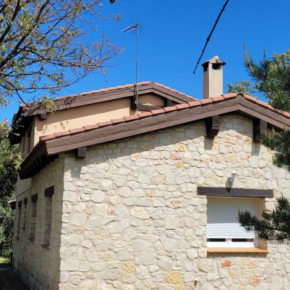 Casa de piedra con techo inclinado en proceso de arreglo de aleros, mejorando la durabilidad y la protección contra el clima